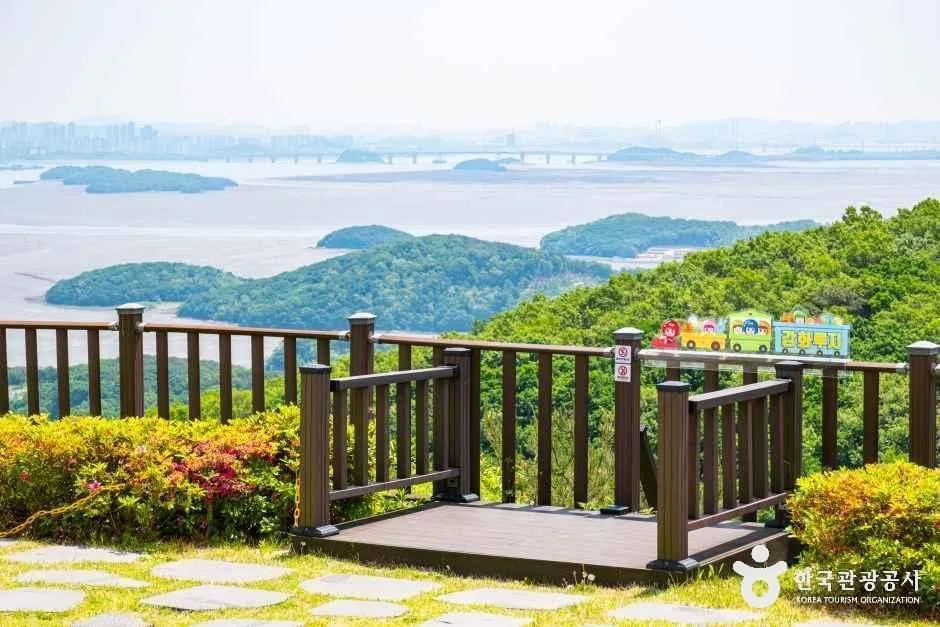 산 위 나무 난간 너머로 강화 남쪽 바다와 갯벌, 크고 작은 섬들이 흐릿하게 펼쳐진 전망