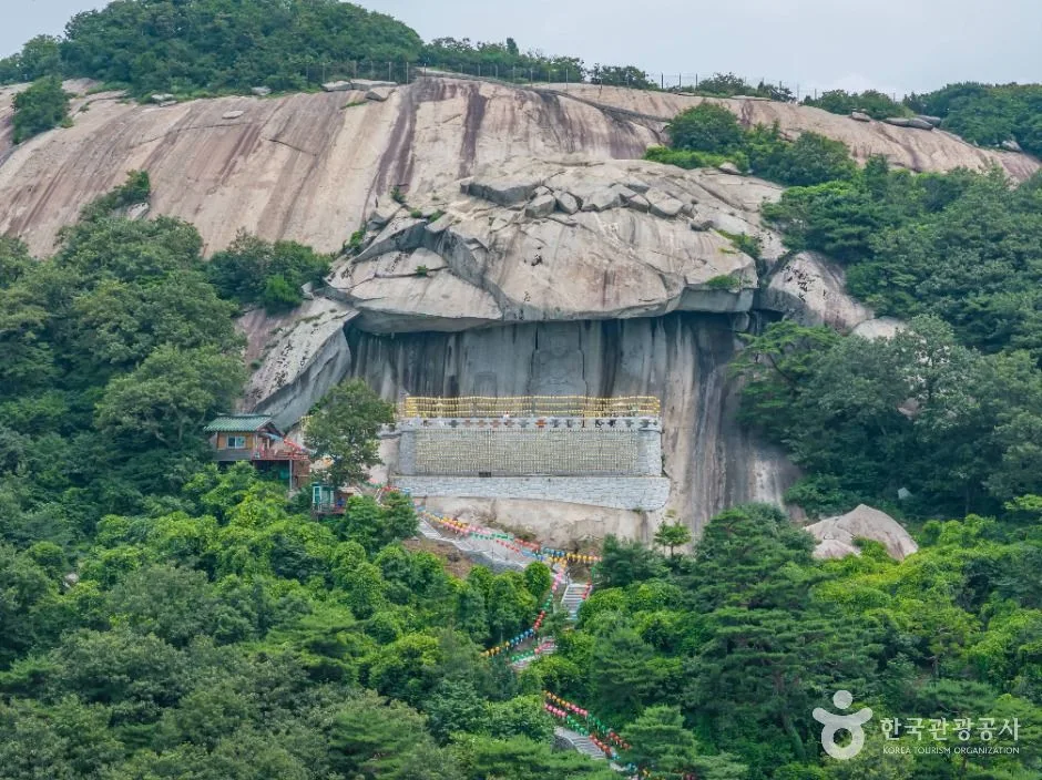 숲이 우거진 낙가산 위로 거대한 바위 절벽이 드러나고 그 아래 노란 연등 줄을 두른 마애관음 기도처가 보이는 보문사
