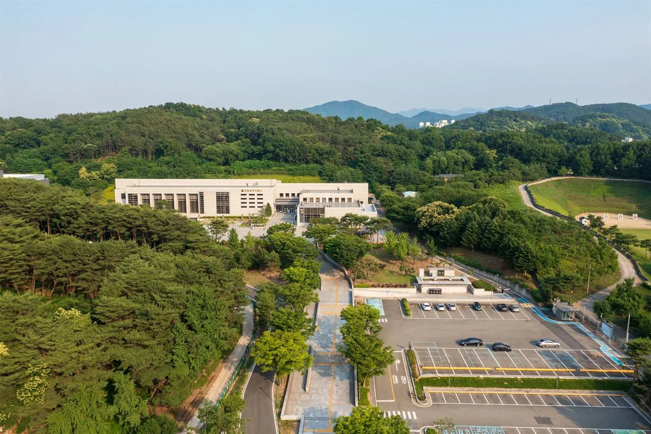 숲으로 둘러싸인 낮은 언덕에 길게 자리한 박물관 건물과 그 앞의 너른 주차장을 위에서 내려다본 국립공주박물관