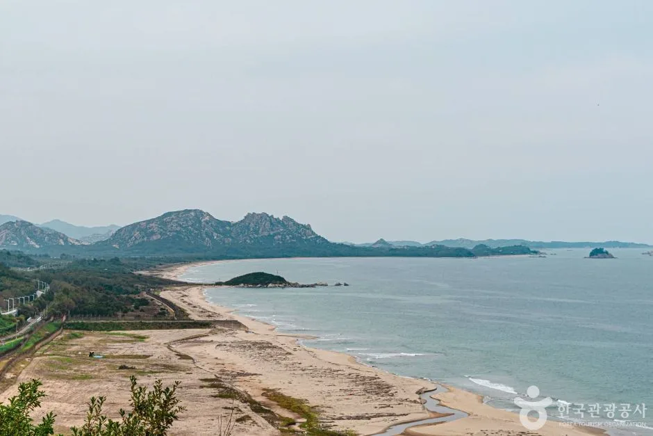 전망대에서 내려다본 동해안, 하얀 백사장이 북쪽으로 길게 이어지고 그 너머 바다 위로 바위섬과 금강산 자락 봉우리들이 보인다