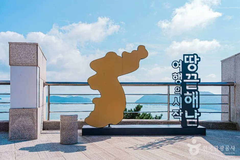전망대 난간 앞에 한반도 모양 조형물과 「땅끝해남 여행의 시작」 글씨가 서 있고 뒤로 푸른 바다와 섬이 보이는 모습