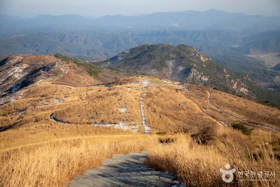 억새 덮인 고원을 가로지르는 길 너머로 바위 봉우리와 겹겹의 산줄기가 펼쳐진 황매산 정상부
