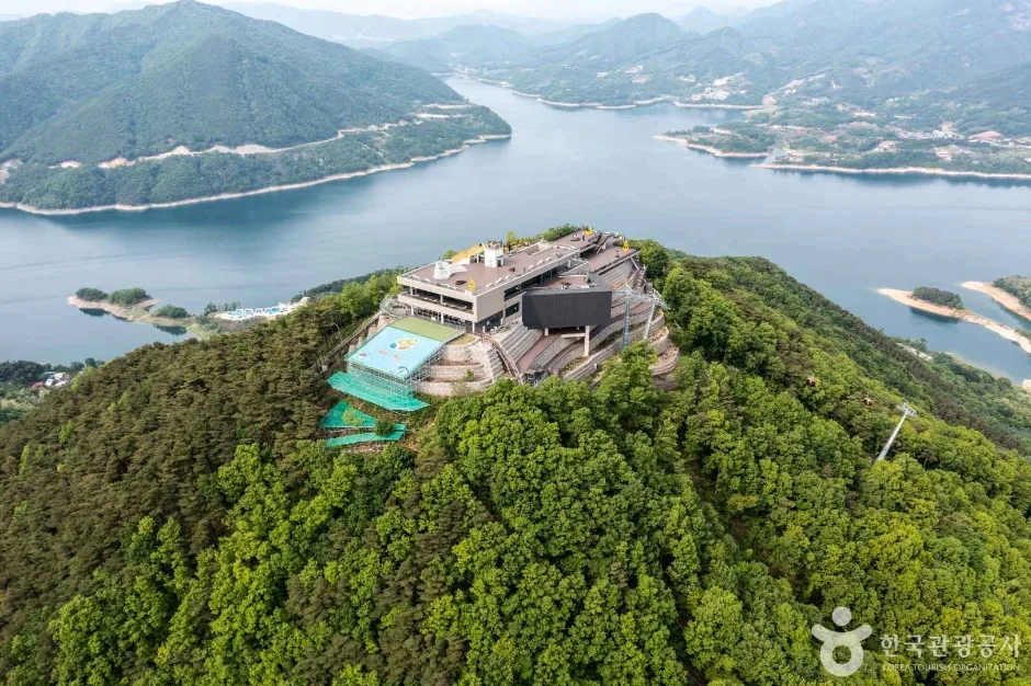숲으로 덮인 산꼭대기에 케이블카 상부 승강장 건물이 앉아 있고 그 뒤로 섬이 점점이 떠 있는 청풍호가 펼쳐진 모습