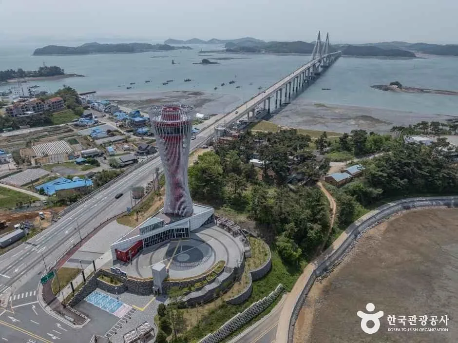 붉은 줄무늬 전망 타워가 바닷가 언덕에 솟고 그 옆으로 원산안면대교 사장교가 바다를 건너 섬들 사이로 뻗은 모습