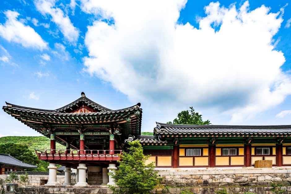 파란 하늘과 흰 구름 아래 단청을 입힌 불갑사 누각과 긴 요사채가 돌기단 위에 서 있는 모습